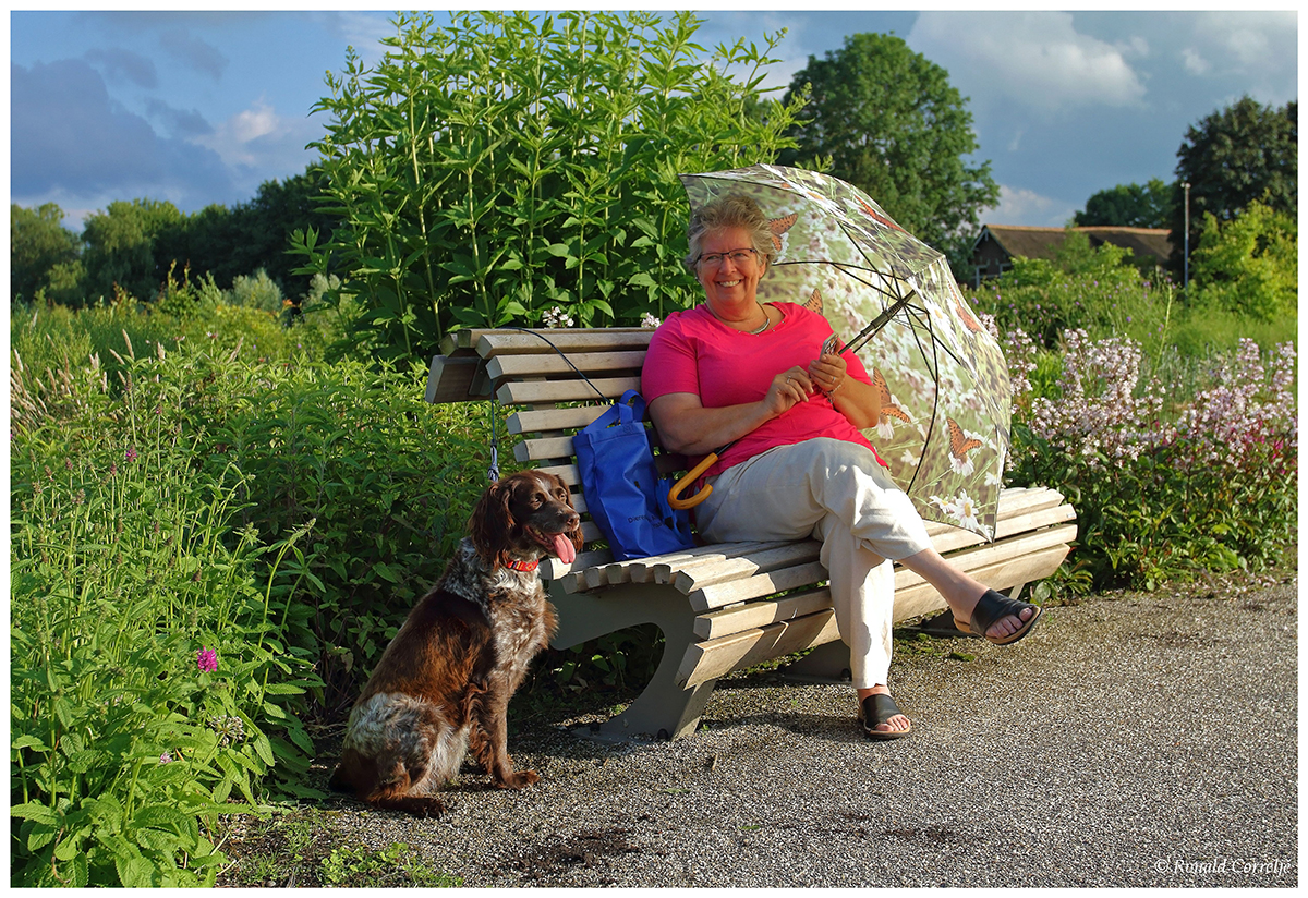 dame met hond en parasol zittend op bankje in de tuin